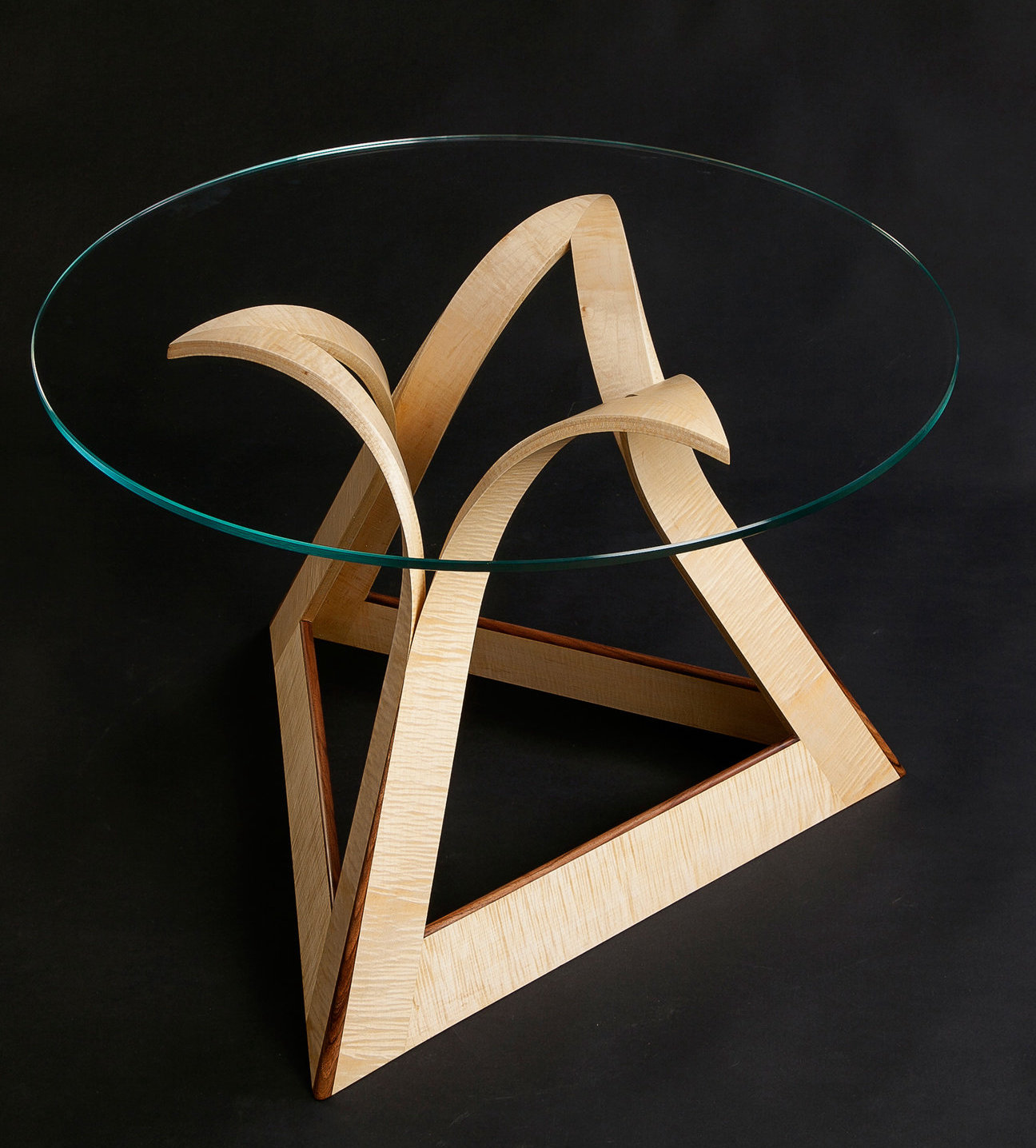 Huw Edwards Jones, a Vesuvius coffee table. Solid ripple sycamore and English walnut with a circular glass top. Base inset with a craft gilt mark numbered 272 for excellence in construction and design from The Worshipful
